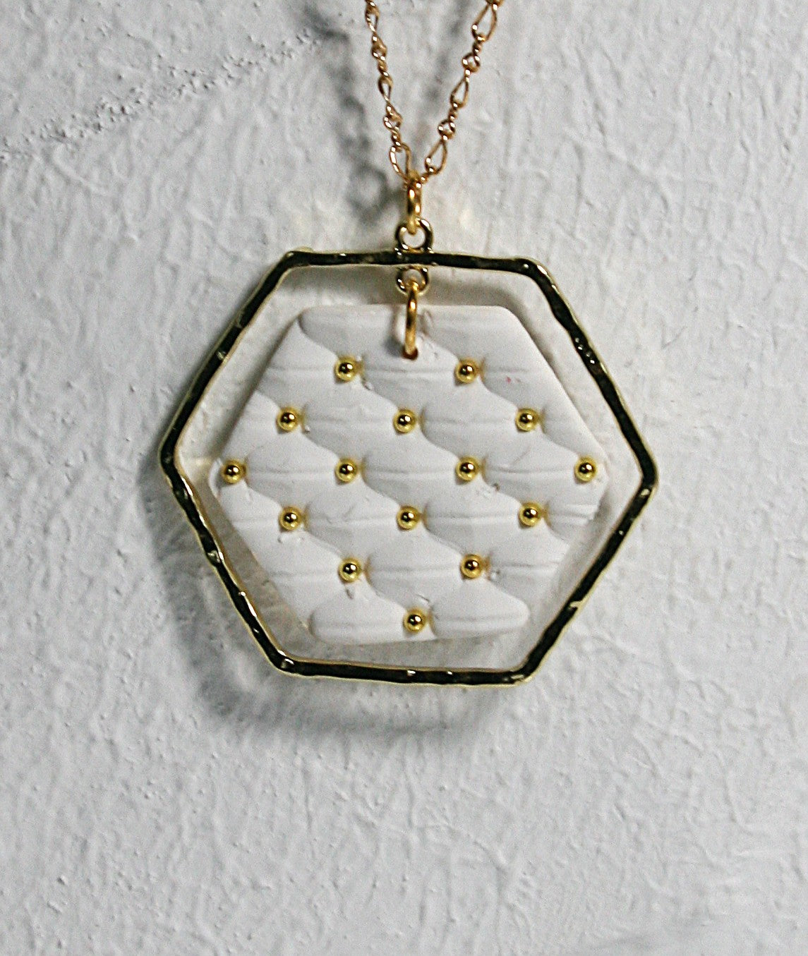 White polymer clay with quilted texture hexagon pendant hanging on a gold plated filigree chain