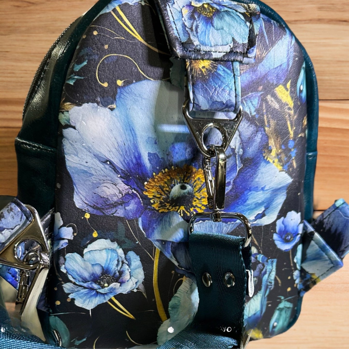 Small blue floral sling bag featuring a blue poppies vinyl exterior, a durable nylon webbing adjustable strap, and silver hardware. Designed for convenience and style, this compact sling includes an interior slip pocket for easy organization. Perfect for hands-free carrying while adding a floral touch to any outfit.