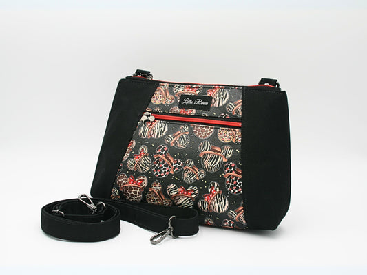 Mickey-inspired animal print crossbody bag with a black canvas exterior and a coordinating red and white cotton interior lining. This medium-sized crossbody purse features an interior zipper pocket, exterior zipper pocket, and an adjustable crossbody strap for hands-free convenience. Perfect for Disney fashion lovers, travel bags, theme park accessories, and everyday use.
