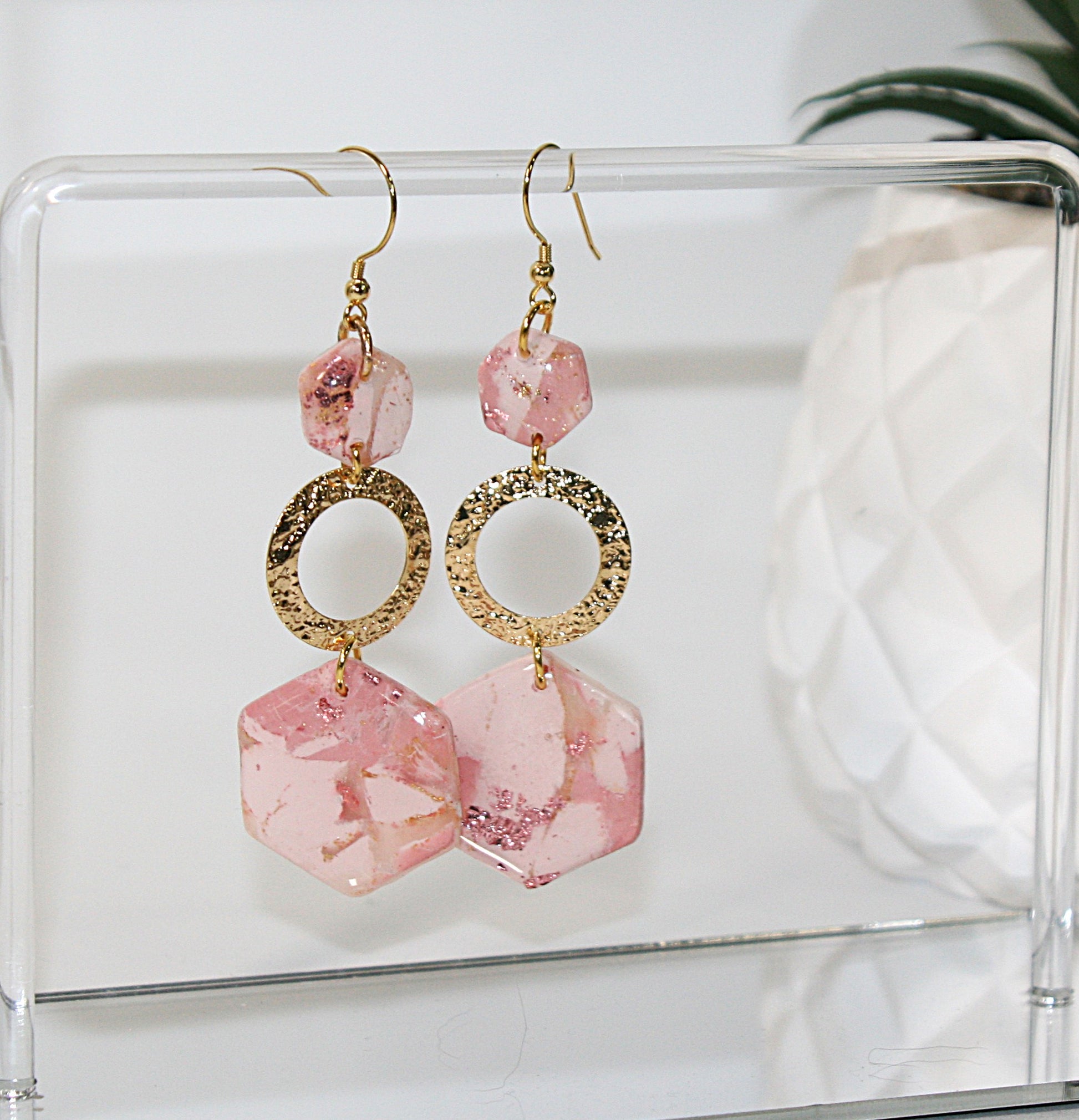 Pink and gold earrings on a clear stand with a white background