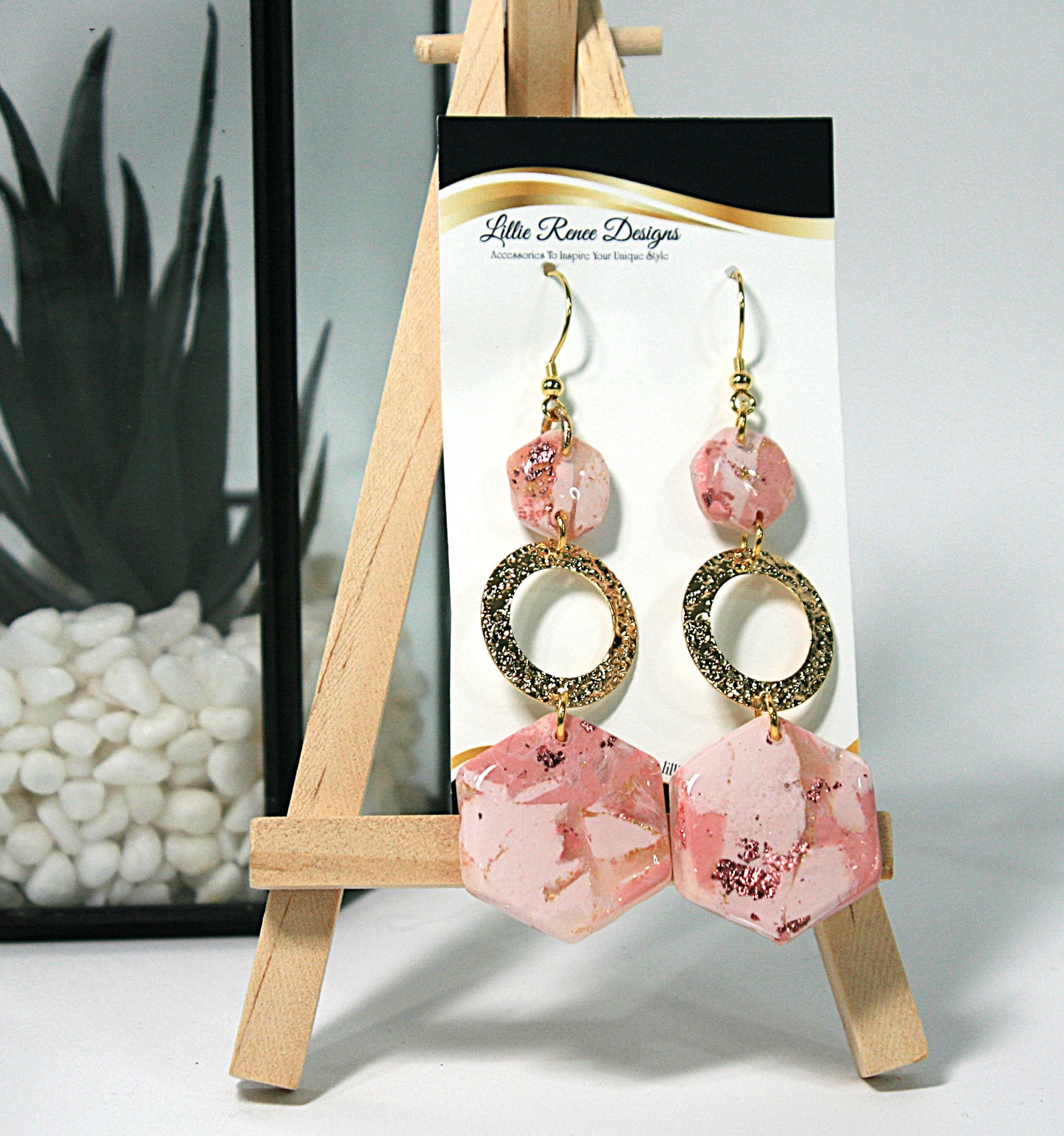 Pink earrings with gold accents on a wooden stand against a neutral background
