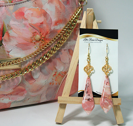 Pink teardrop earrings on a stand with a floral  purse in the background