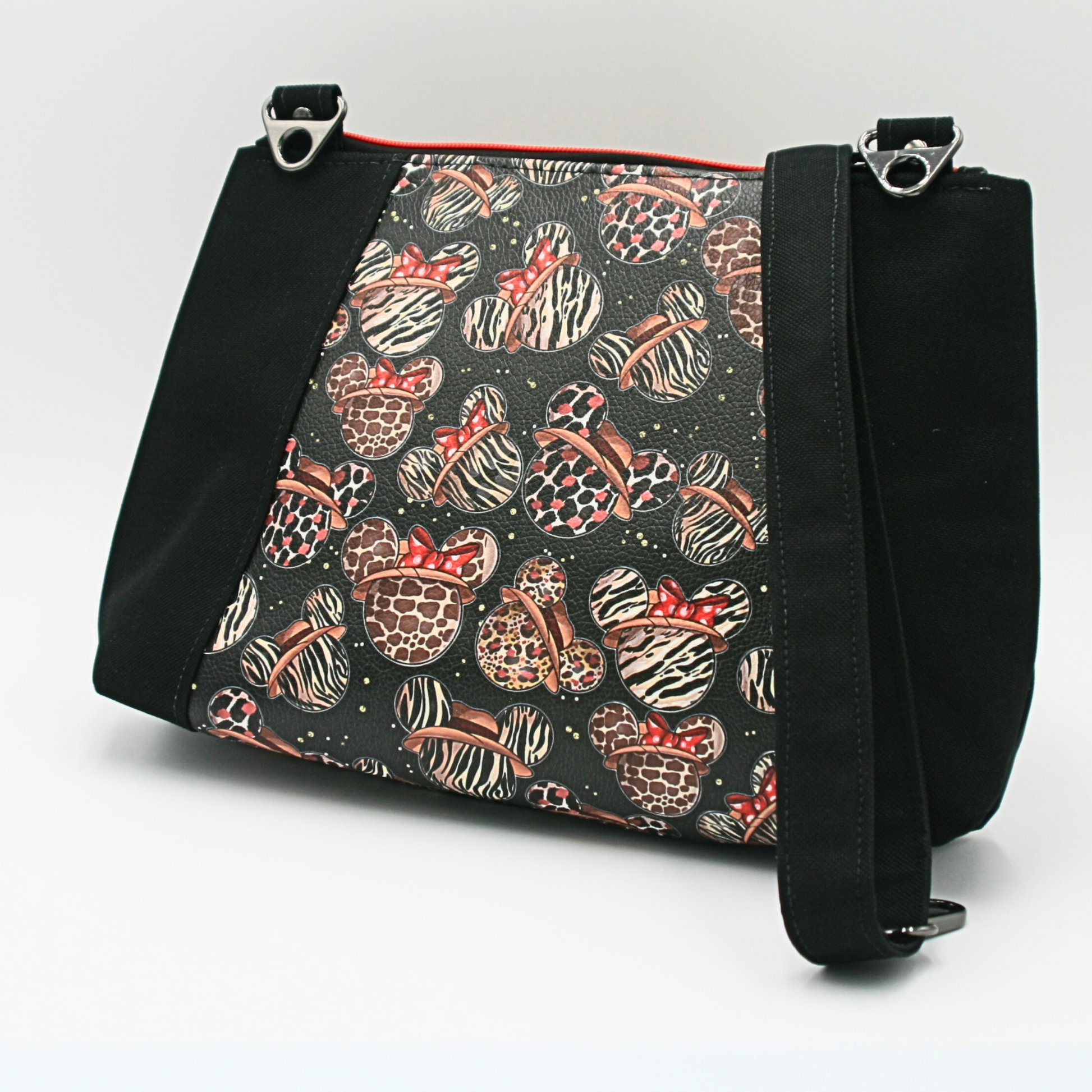 Mickey-themed crossbody purse with animal print vinyl and black canvas. Lined with a coordinating red and white cotton fabric, this medium crossbody handbag offers a spacious interior zipper pocket, an exterior zipper compartment, and an adjustable crossbody strap for comfort and versatility. A must-have for Disney fans, stylish travel bags, and unique fashion accessories.